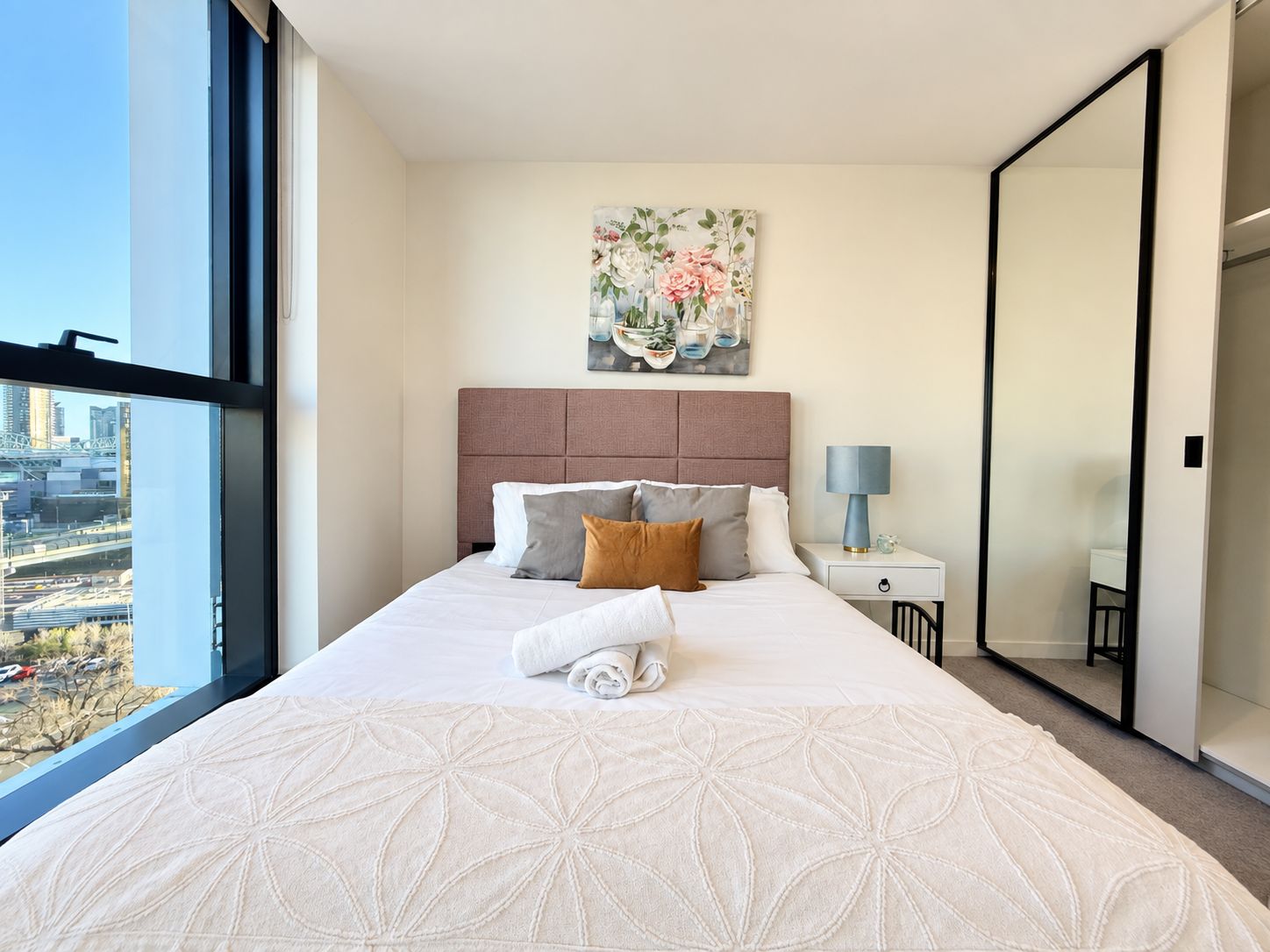 Habitación de hotel con una cama grande, una mesita de noche, una lámpara, un cuadro y vistas a la ciudad.