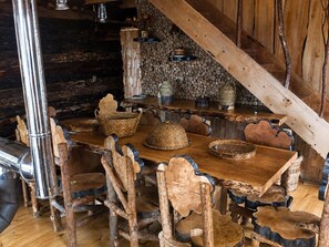 A rustic dining area with a wooden table and chairs, surrounded by a stone wall and wooden beams.