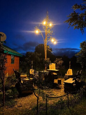 An outdoor seating area with tables and chairs, surrounded by trees and a building with a green roof.