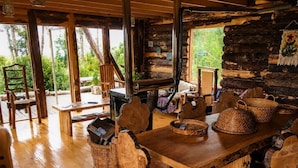 Un coin repas rustique, avec une grande table et des chaises en bois, entouré de murs en rondins et offrant une vue sur la verdure environnante.