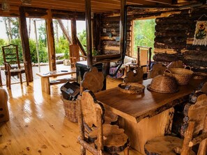 Un'area pranzo rustica in legno con un grande tavolo e sedie, circondata da pareti in legno e vista su del verde all'esterno.