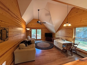 A cozy cabin interior with a sofa, dining table, and chairs, wooden walls, and a ceiling fan.