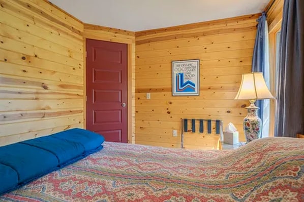 Una habitación de madera con una cama, una puerta roja y un letrero en la pared.