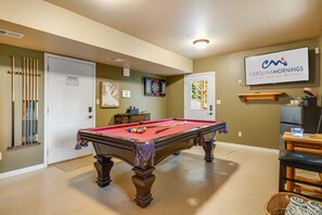 Une table de billard dans une pièce où l’on trouve un jeu de fléchettes, un téléviseur diffusant une émission intitulée « Carolinamornings, locations de vacances de luxe », et une porte sur laquelle est apposée une pancarte indiquant « ENTRÉE INTERDITE ».