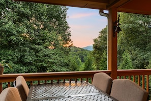 Un espace extérieur aménagé, abrité et doté de tables et de chaises, offrant une vue sur une forêt dense et une chaîne de montagnes.