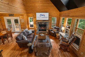L’intérieur chaleureux d’un chalet avec une cheminée, des meubles en cuir et une enseigne indiquant « Carolina Mornings Luxury Vacation Rentals ».
