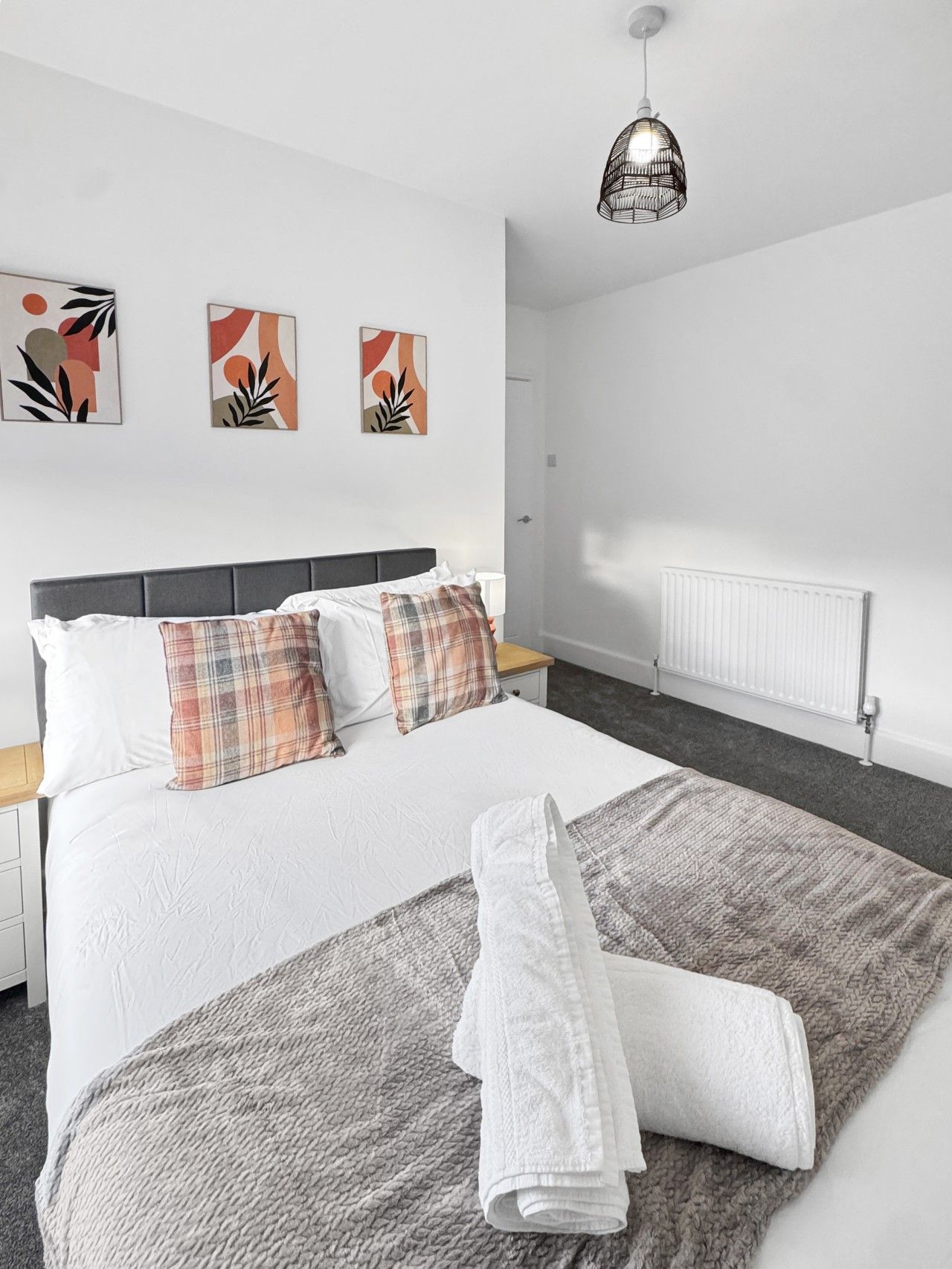 A hotel room with a bed, a bedside table, a lamp, and a radiator.