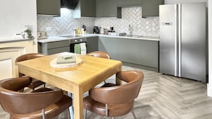 Uma cozinha moderna com mesa de jantar de madeira, cadeiras de couro marrom, geladeira de aço inoxidável e painel de backsplash em padrão herringbone.