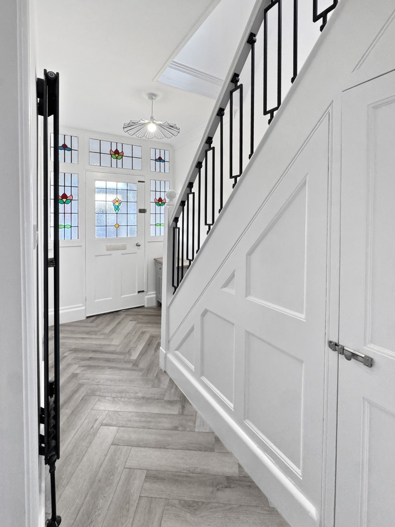 A hallway with a wooden herringbone floor, white doors, and a black metal railing.