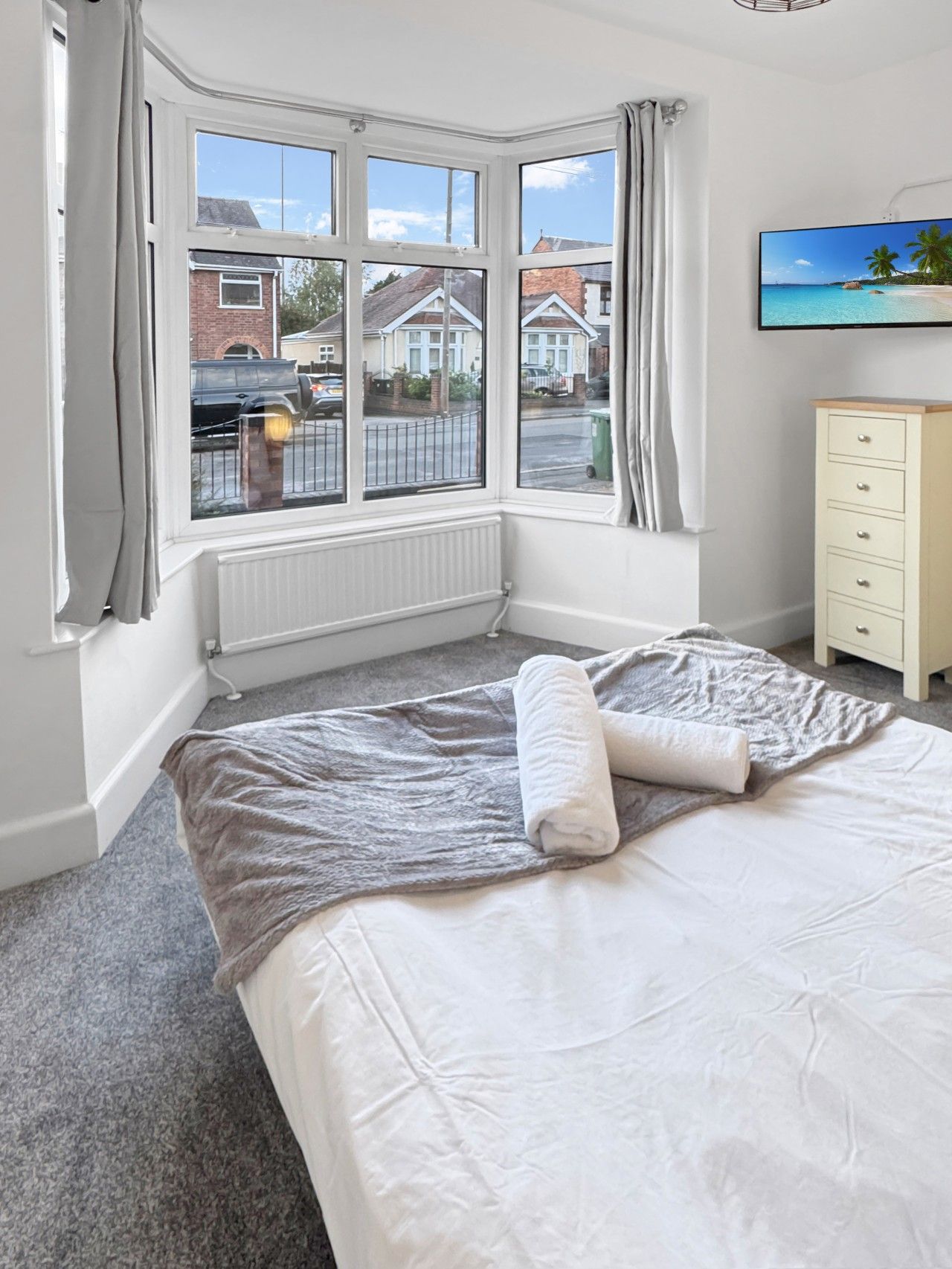Una camera da letto con un letto grande, un termosifone, una finestra con tende e una televisione a parete, con vista sui case.