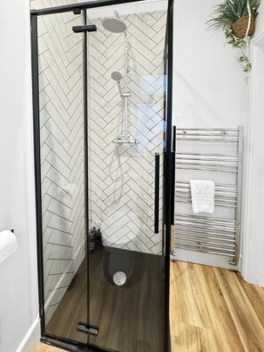 A glass-enclosed shower with a herringbone tile pattern on the walls, a wooden floor, and a towel rack with a white towel. - Sleeps 8 4 bed Heanor with Garden & Driveway (Heanor)