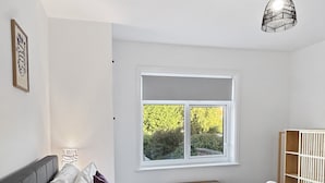 Quarto com cama, mesa de cabeceira, luminária, janela com vista para vegetação e luminária pendente.