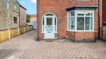 A two-story brick house with a front door, a bay window, and a number plate.