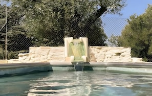 Ein Pool mit Wasserfall, umgeben von einer Steinmauer und einem Drahtzaun.