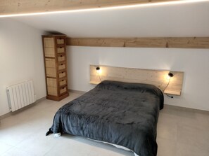A bedroom with a bed, a wooden headboard with lights, a radiator, and a tall wooden cabinet.