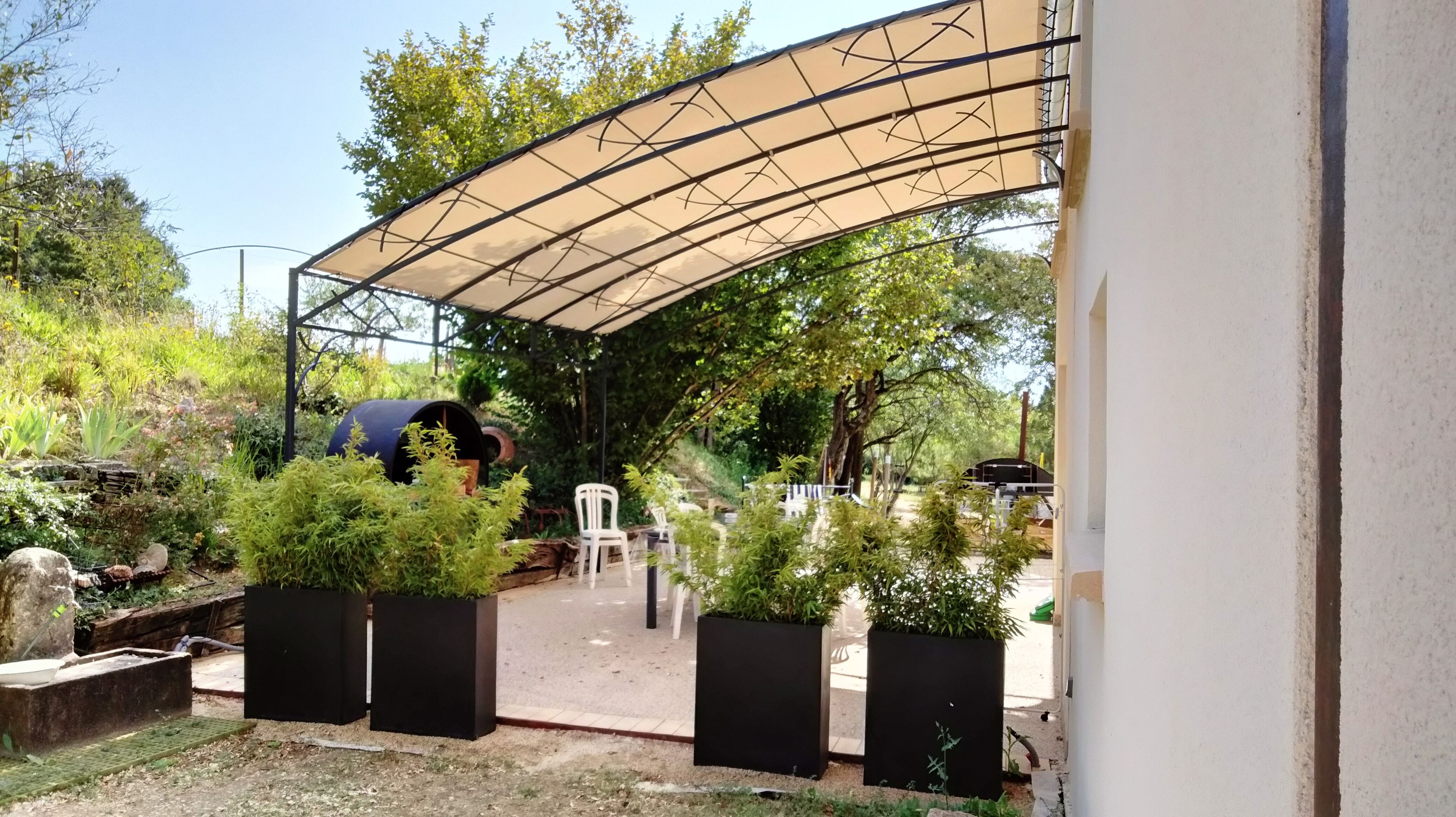 An outdoor patio area with a curved canopy, potted plants, and a seating arrangement.