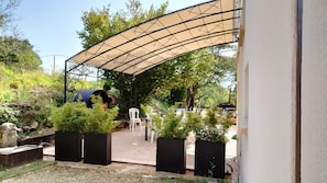 Ein Außenbereich mit Terrasse, einer gewölbten Markise, Pflanzgefäßen und einer Sitzgruppe.