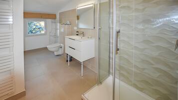 Ein modernes Badezimmer mit Duschkabine aus Glas, einem weißen Waschbecken und einer Toilette.