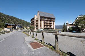 Ein mehrstöckiges Gebäude mit Balkonen, eine gepflasterte Straße davor und ein klarer Himmel.