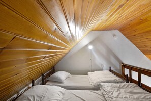 Ein kleiner Raum mit schrägem Dach, zwei Betten und einer weißen Wand.