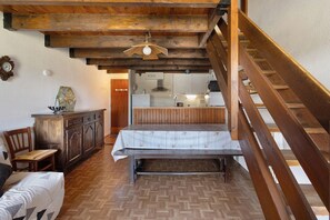 Ein rustikales Interieur mit einer Holztreppe, einem Essbereich inklusive Tisch und Stühlen sowie einer durch eine offene Tür erkennbaren Küche.