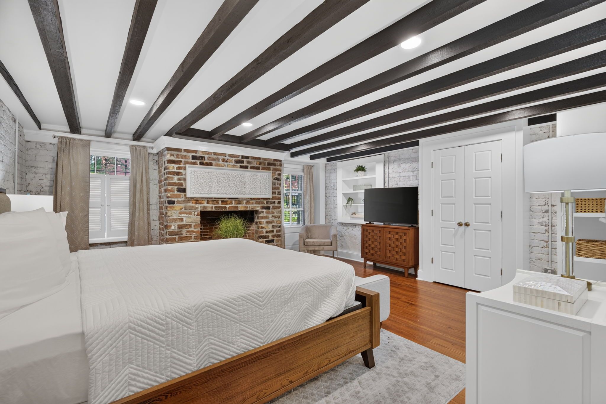 A bedroom with a large bed, a brick fireplace, a television, and a wardrobe.