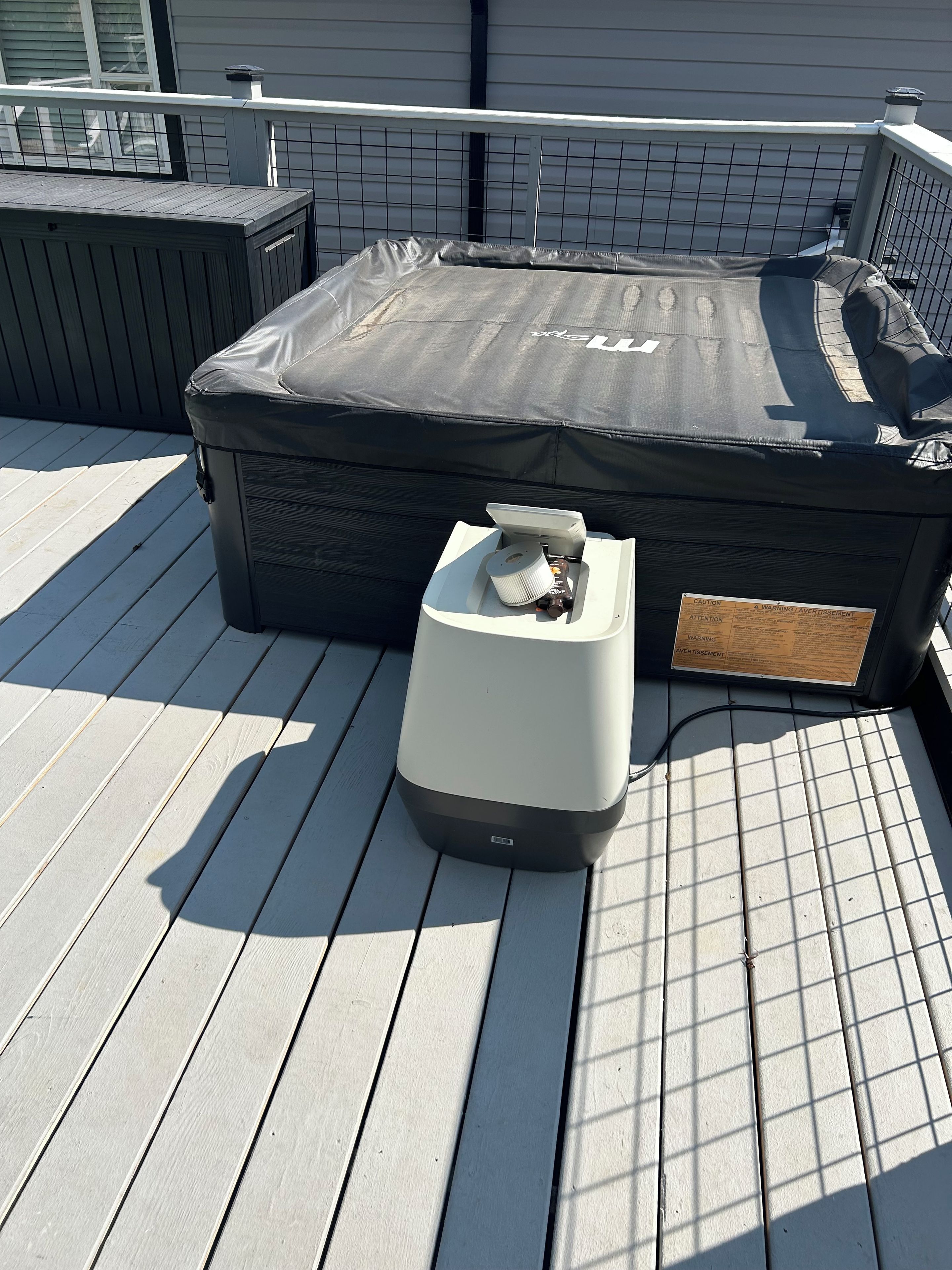 Ein Whirlpool auf einer Holzterrasse mit Sicherheitsabdeckung, einem tragbaren Heizgerät und einem Warnschild.