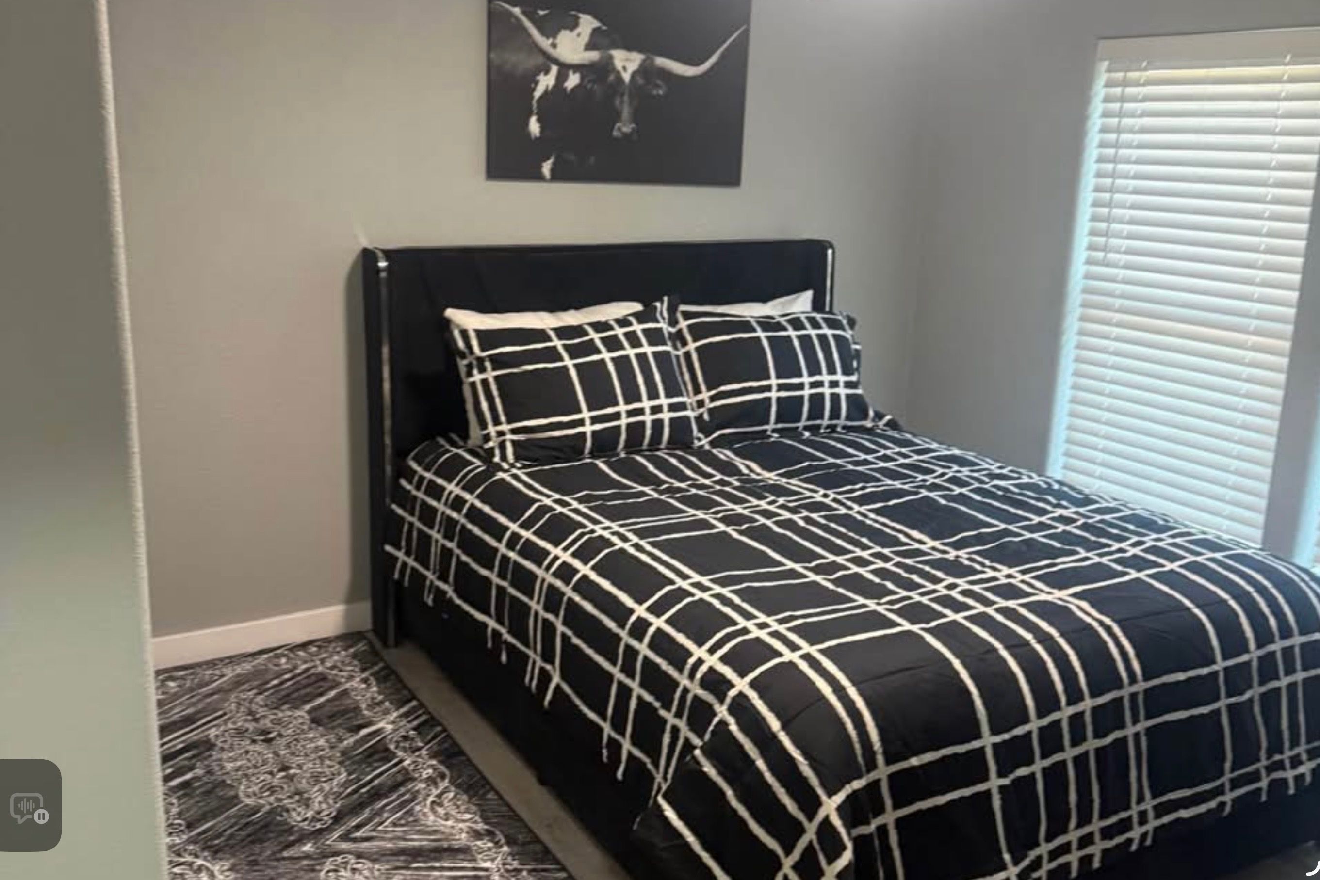 Een slaapkamer met een bed, een hoofdeinde, een aan de muur hangend kunstwerk en een raam met jaloezieën.