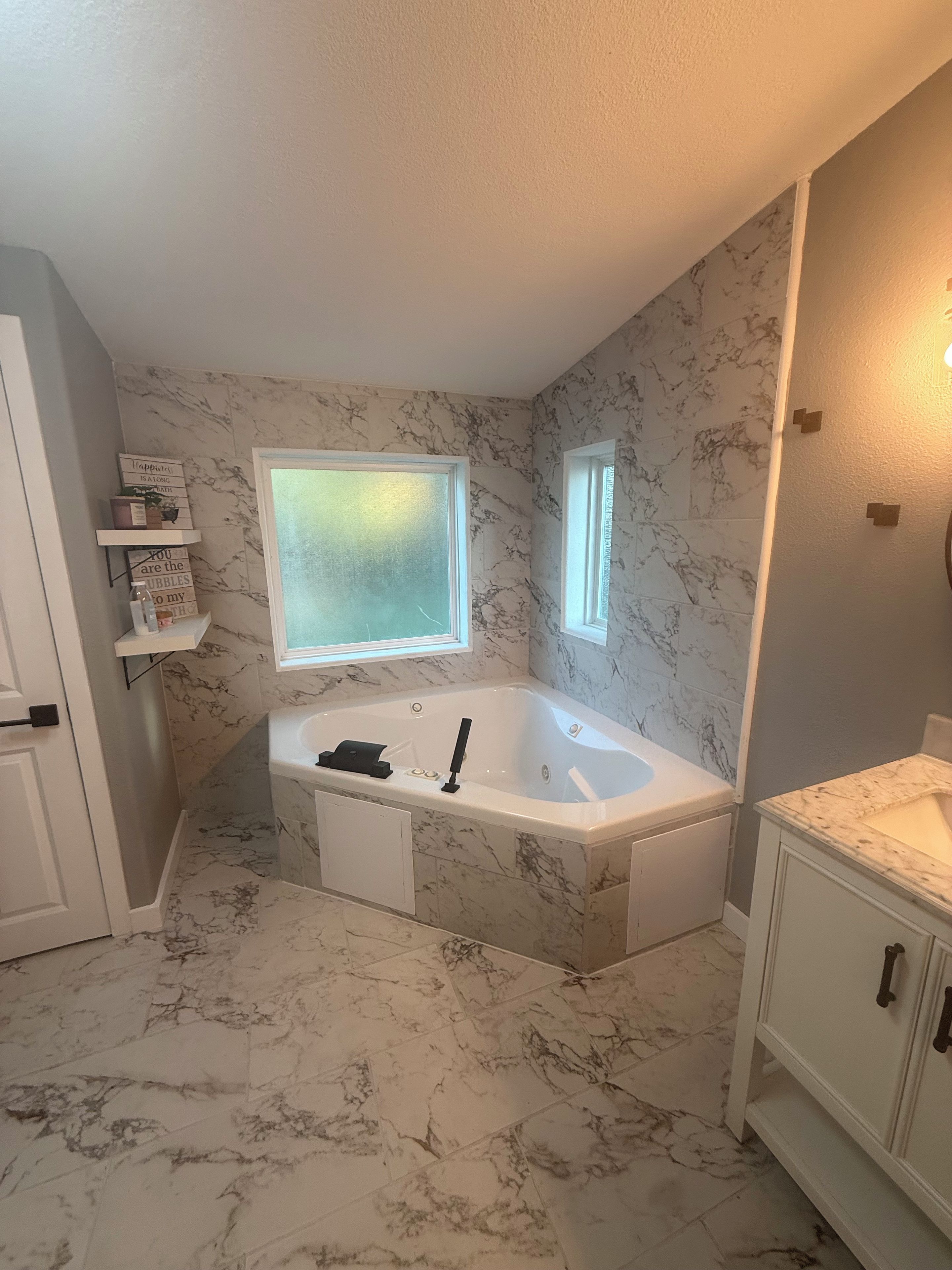 Ein Badezimmer mit Marmorboden, einer freistehenden Badewanne, einem Waschtisch und einem Fenster über der Badewanne.