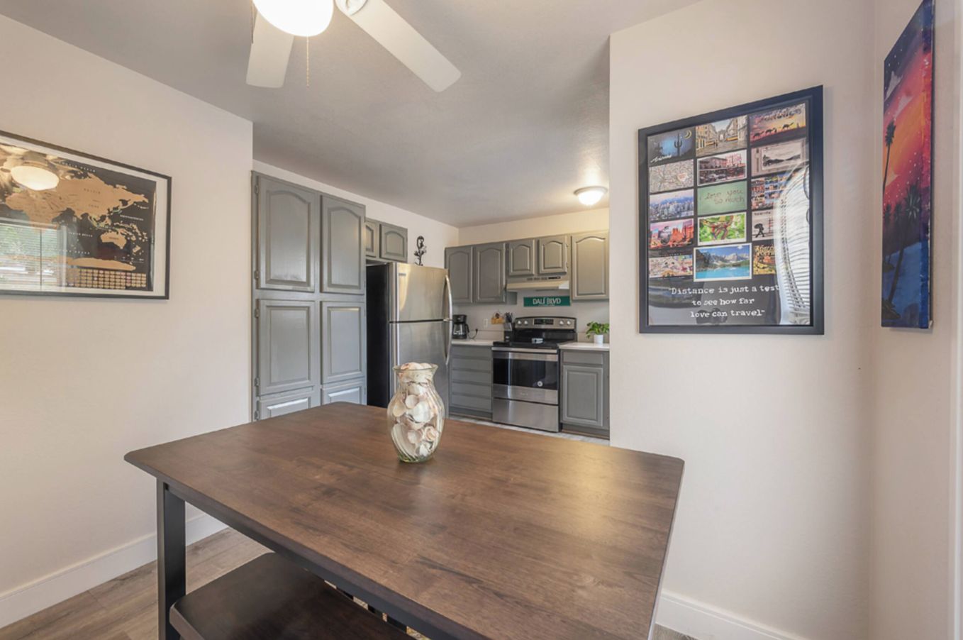 A modern kitchen with grey cabinets, a stainless steel refrigerator, and a dining area with a wooden table and a vase.