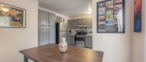 A modern kitchen with grey cabinets, a stainless steel refrigerator, and a dining area with a wooden table and a vase.