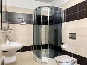 Un bany modern amb dutxa tancada per vidre, un lavabo blanc i un vàter.