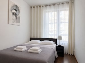 Un llit ben fet amb llençols blancs, una làmpada de nit i una finestra amb cortines de transparència.