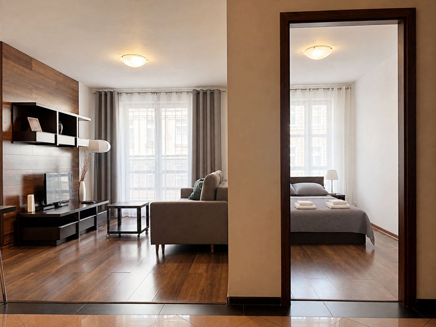 Una habitación de hotel moderna con piso de madera, un sofá, una cama, un escritorio y un televisor.