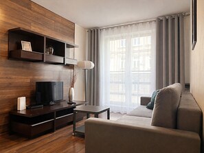 Ein modernes Wohnzimmer mit Fernseher, einem kleinen Tisch, einer Couch und einem großen Fenster mit Vorhängen.