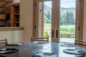 A dining area with a round table, chairs, and a view of a mountainous landscape through open doors. - Weyyakin Home 307- Amazing Home Minutes From Downtown & Skiing (Sun Valley)
