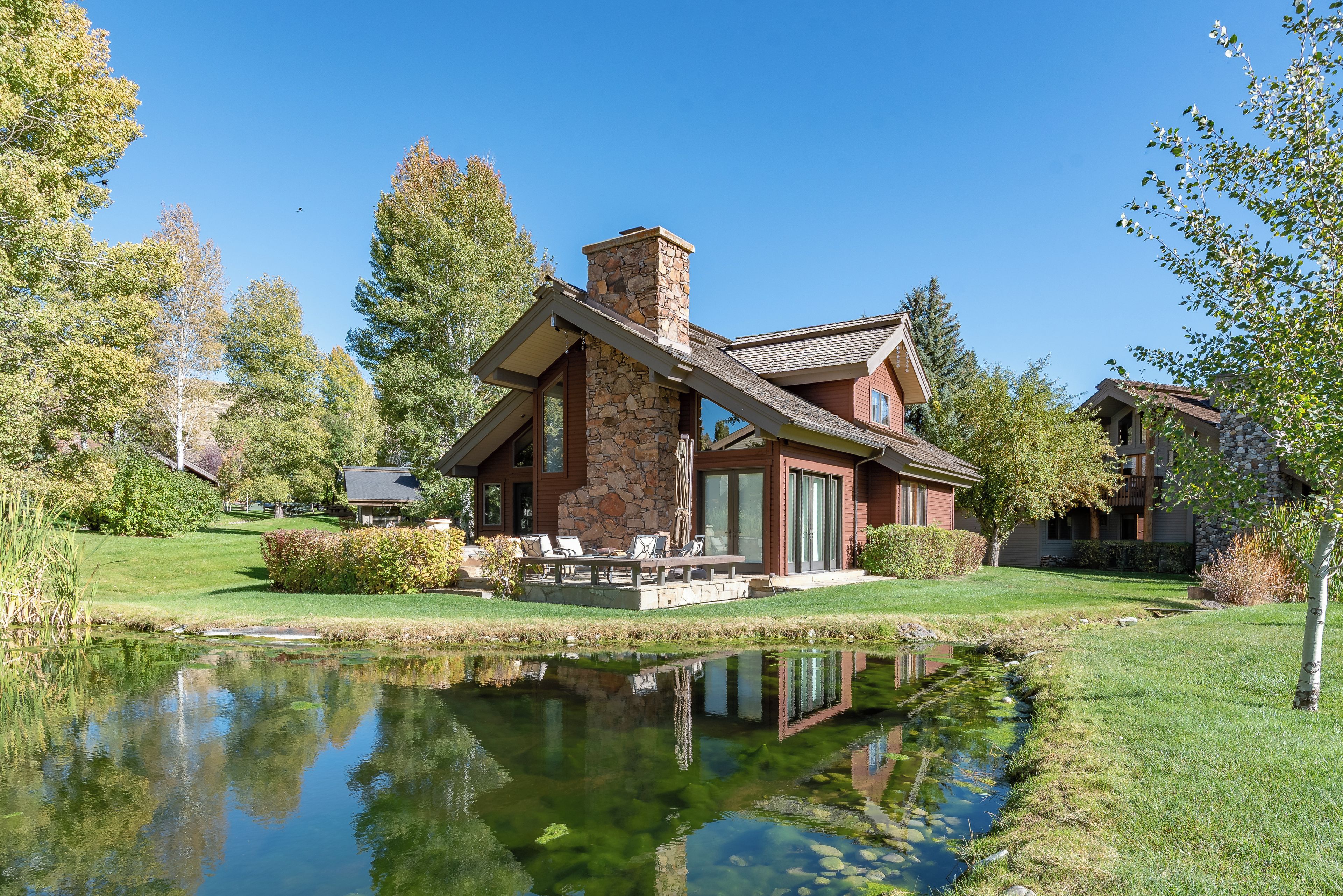 A two-story house with a stone chimney, a pond in front, and a well-maintained lawn.