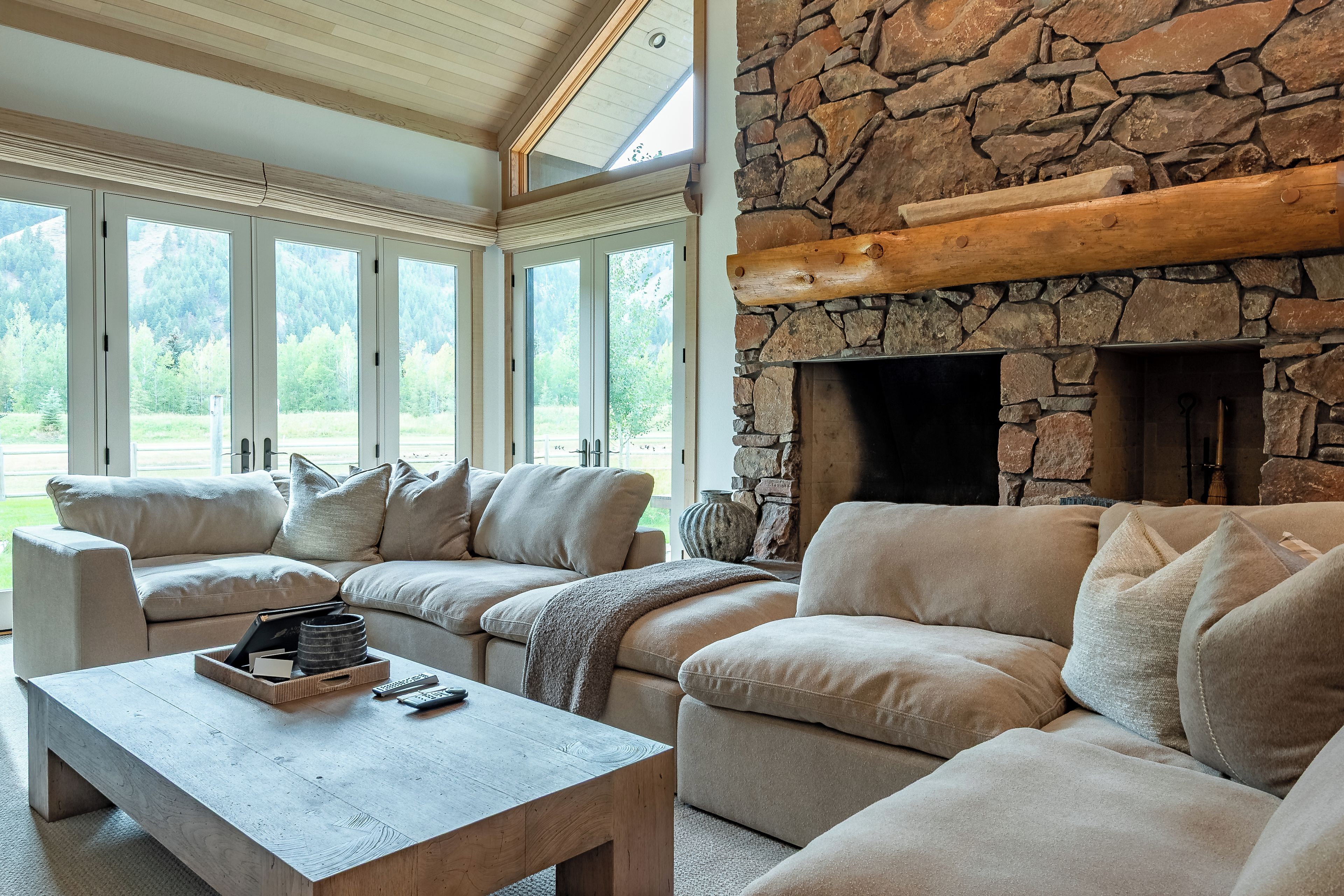 Una sala de estar moderna con chimenea de piedra, ventanas amplias y un sofá modular.