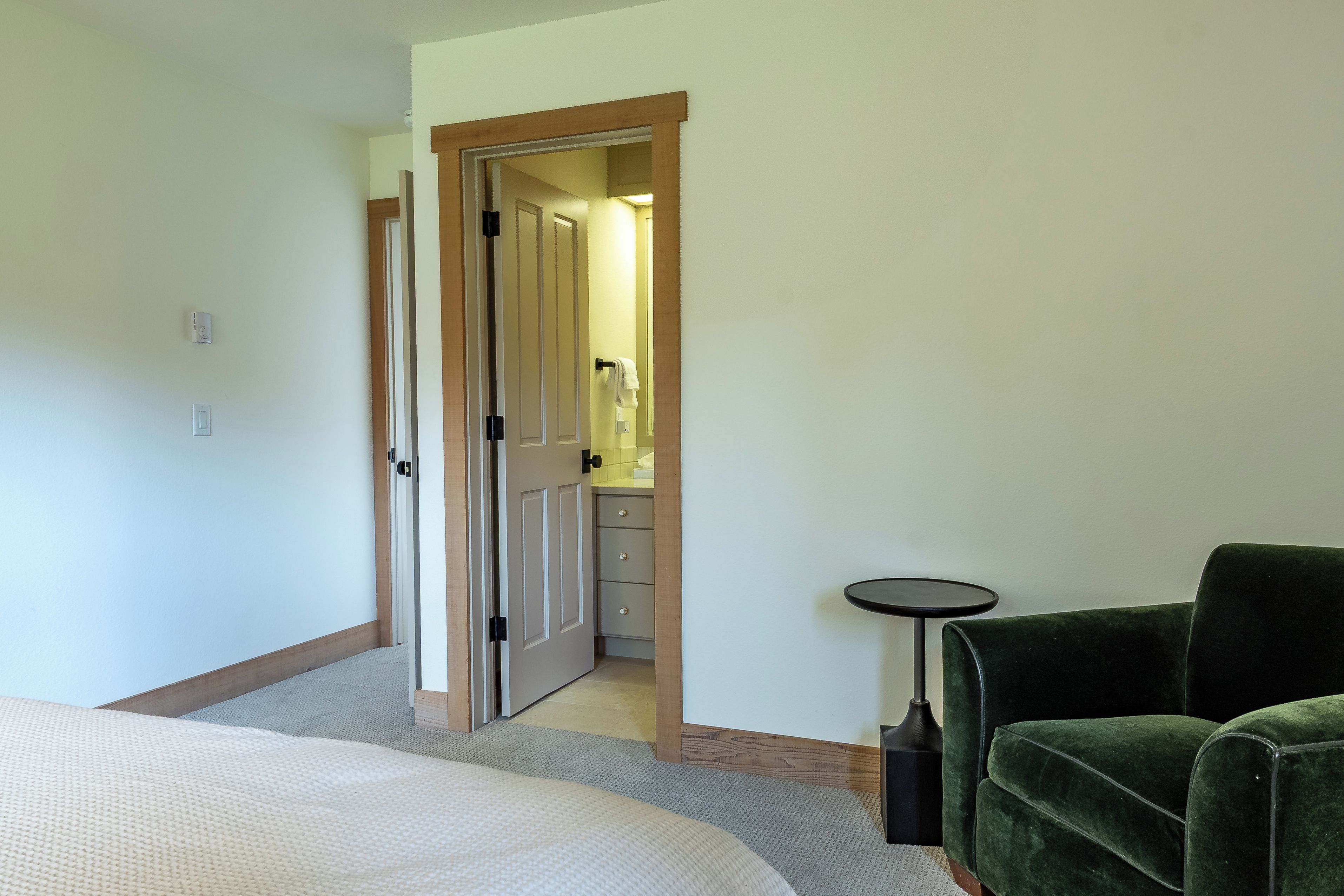 A hotel room with a bed, a green armchair, a small table, and a bathroom visible through an open door.