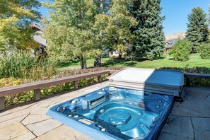 A hot tub on a stone patio with a wooden deck and a view of a residential area with trees and houses. - Weyyakin Home 307- Amazing Home Minutes From Downtown & Skiing (Sun Valley)