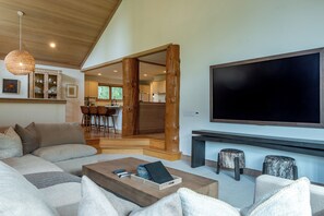 A modern living room with a large flat-screen TV, a fireplace, and a dining area visible through an open doorway. - Weyyakin Home 307- Amazing Home Minutes From Downtown & Skiing (Sun Valley)
