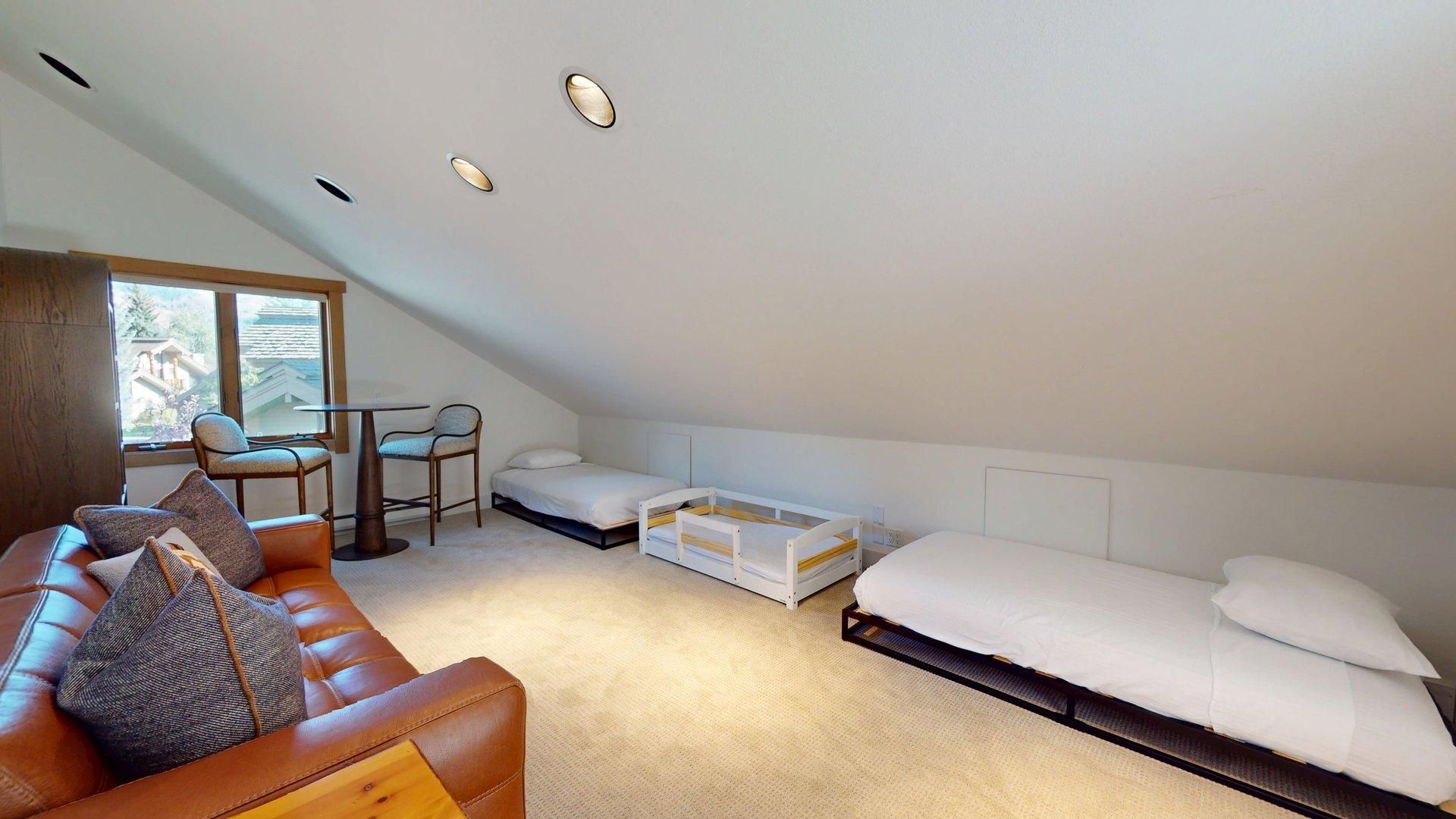 A small, well-lit attic bedroom with a loft bed, a sofa, and a dining table.