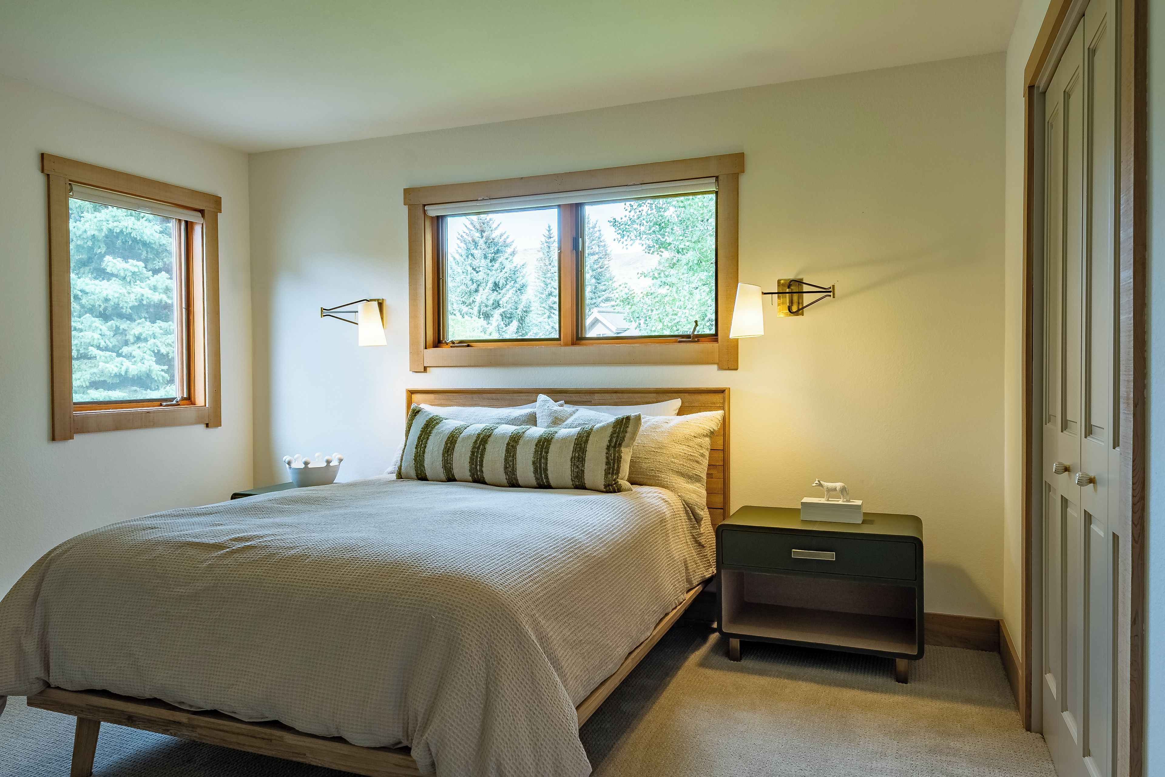 A bedroom with a bed, two bedside tables, a nightstand, and two wall-mounted lamps.