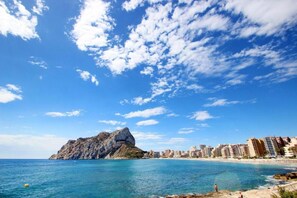A coastal cityscape with a prominent rocky outcrop, beachfront buildings, and clear blue skies. - SUNNY PINES in Calpe Park: family bungalow with pool and playground (Calp)