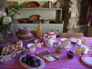 Uma mesa de jantar posta com diversos alimentos, incluindo pão, figos e queijo, e uma garrafa de suco.