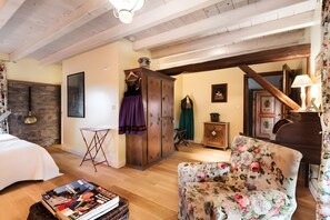 Quarto com cama, um armário de madeira, poltrona estampada e uma mesa com revistas.