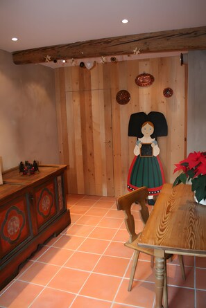 A room with a wooden wall, a wooden table with a chair, a cabinet, and a wall-mounted decoration.