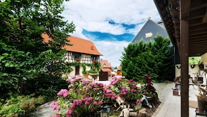 A courtyard with a traditional building, a paved path, and flowering plants. - La Ferme de Sophie - Josepha Room (Kleingœft)