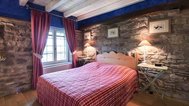 A bedroom with a stone wall, a wooden ceiling, a bed with a red checkered bedspread, two bedside lamps, and a window with curtains. - La Ferme de Sophie - Josepha Room (Kleingœft)