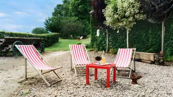 Een patio met grind, twee gestreepte lounge fauteuils en een kleine rode tafel.